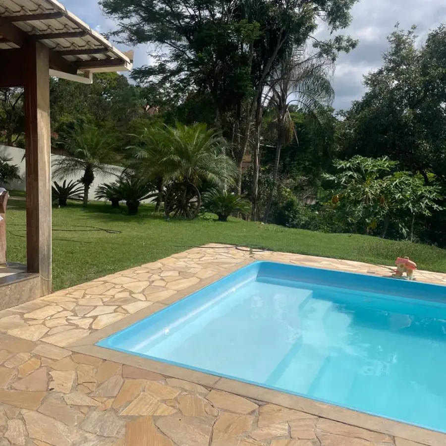 Piscina com deque de pedra e jardim ao redor, vista da área coberta de convívio